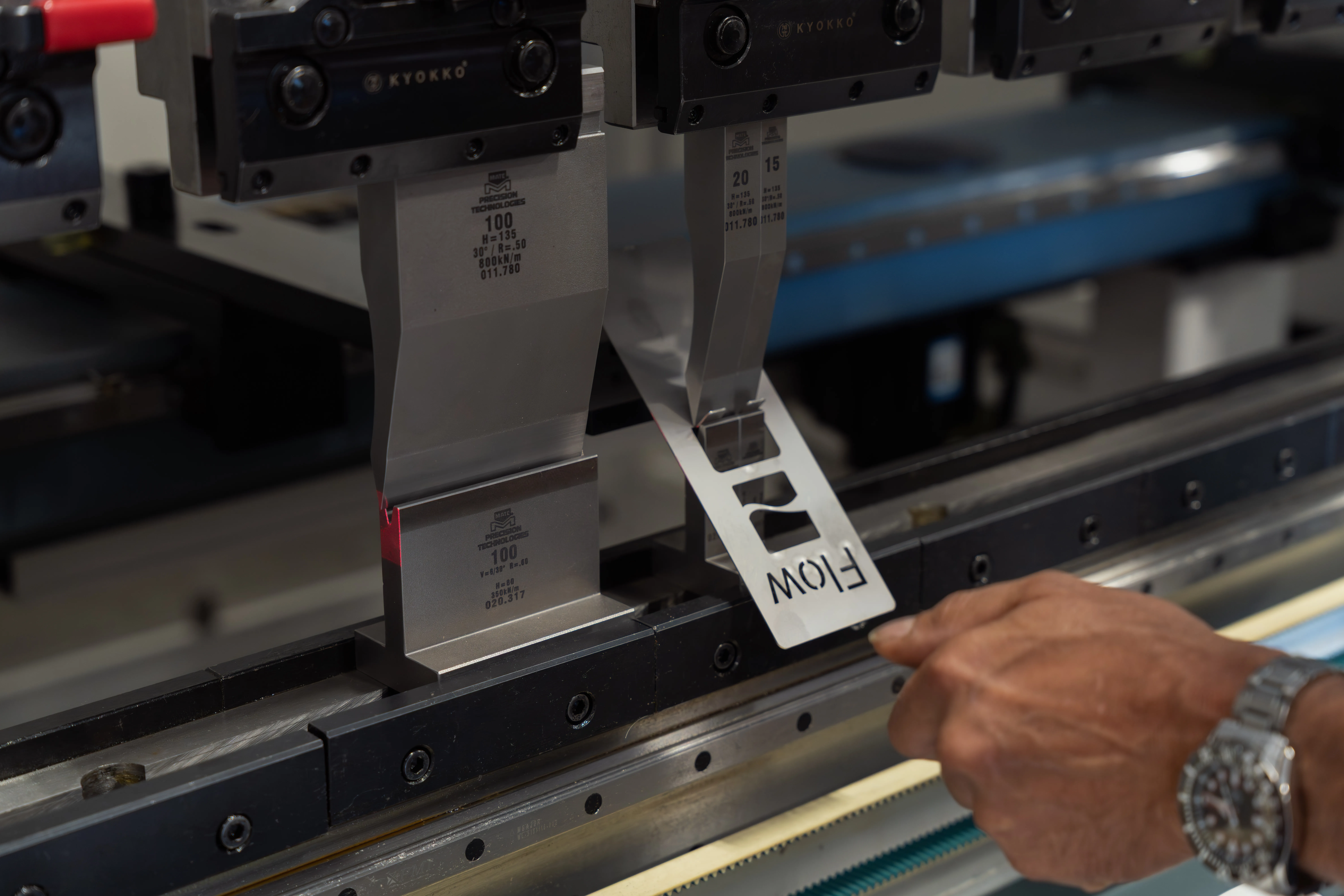 press brake in operation bending a part with the Flow logo and operators hand nearby