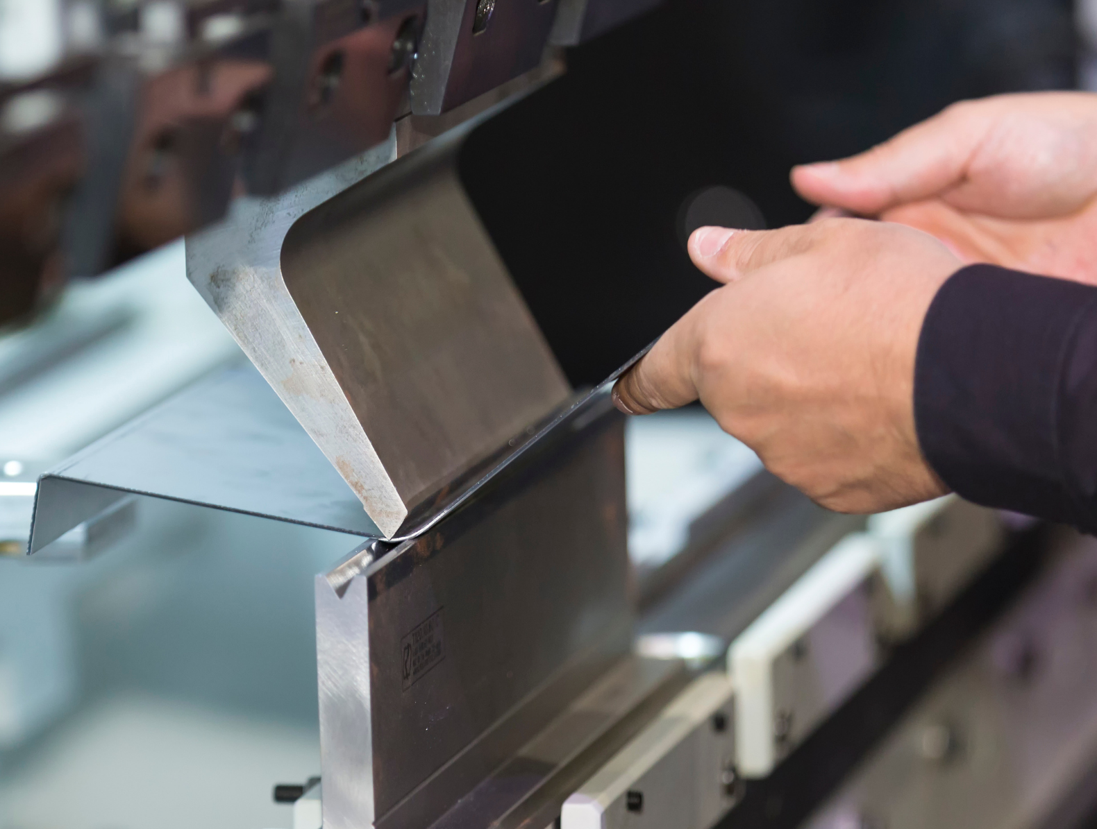 A pair of hands assisting the HyperBend press brake with a bend on a thin metal sheet