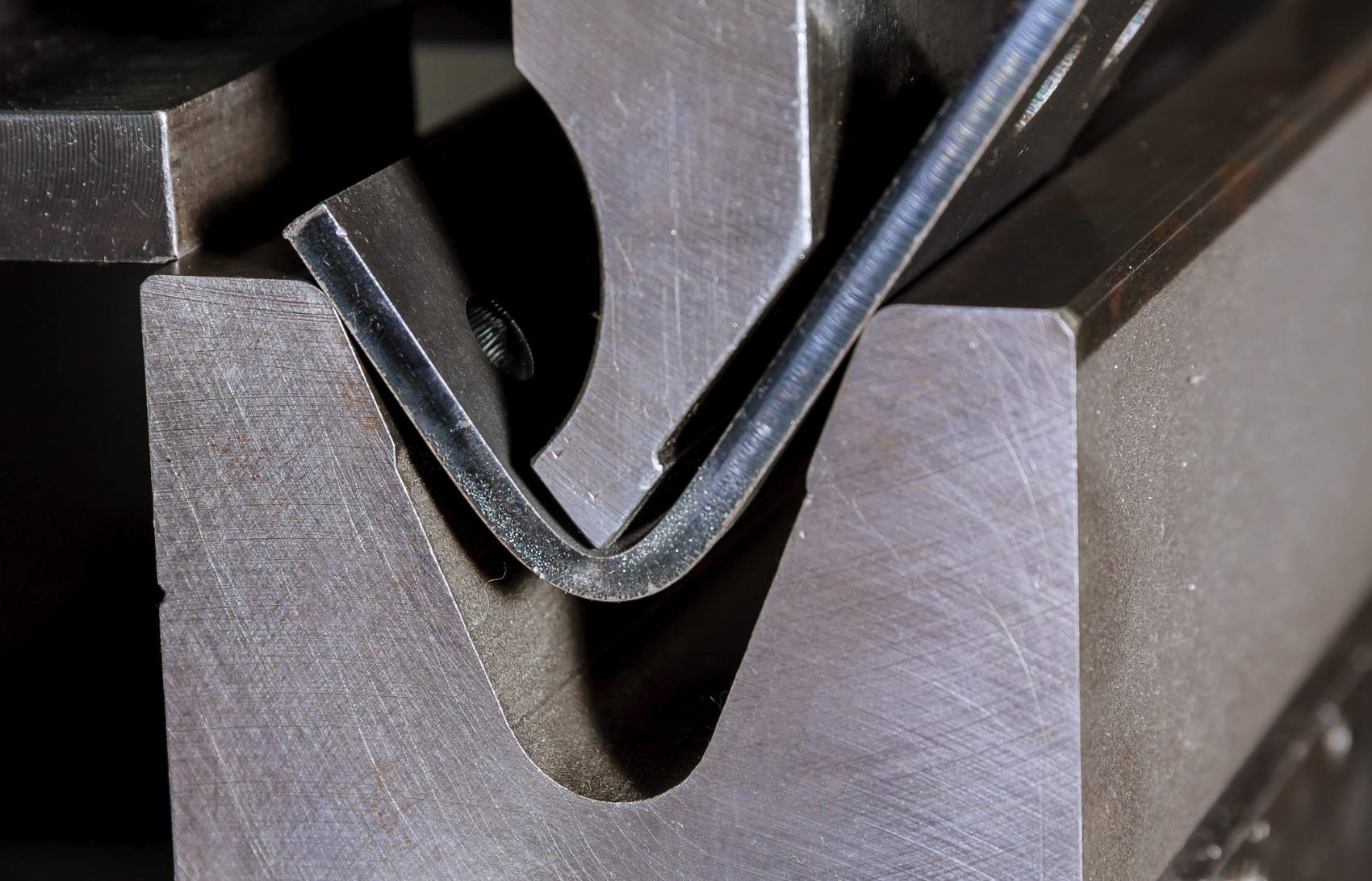 Close up of press brake punch and die assembly in the middle of a bend with a sheet of metal between